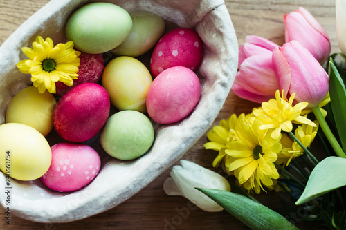 Closeup bunch of fresh flowers and basket with colored eggs placed on lumber tabletop photo