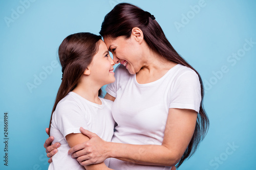 Close up photo adorable amazing pretty two people brown haired mum small little daughter stand close lovely look eyes touch foreheads rejoice wearing white t-shirts isolated on bright blue background