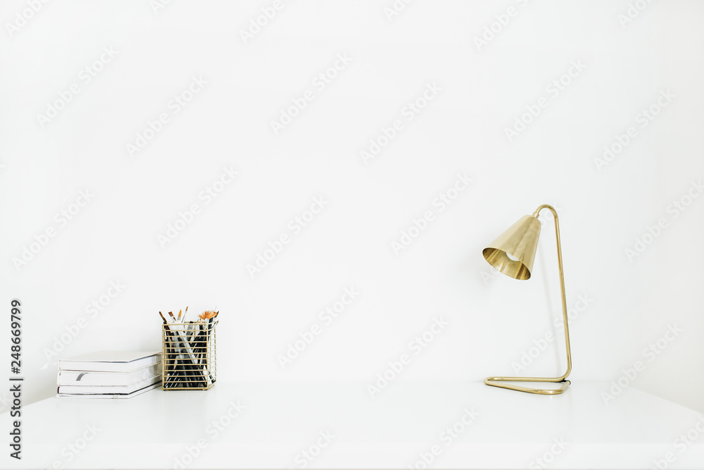 Obraz premium Home office desk workspace with golden lamp, notebooks, stationery on white desktop. Minimal blog, social media, website hero header. Modern interior design concept.