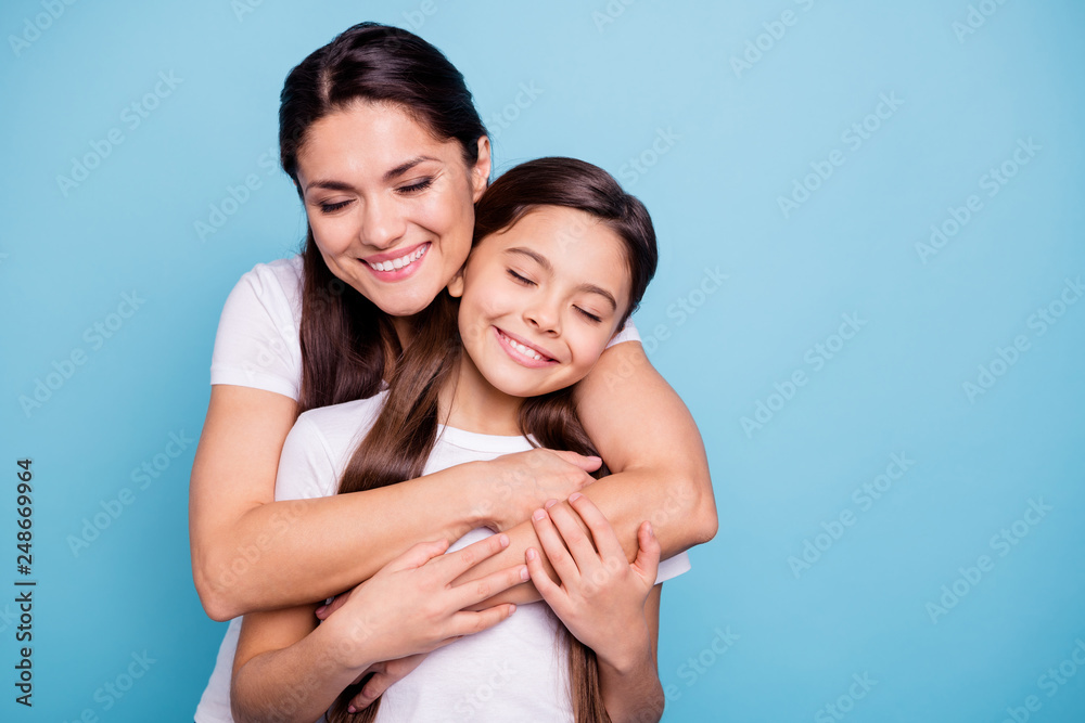 Close up photo pretty two people brown haired mum small little daughter stand hugging piggy back lovely close eyes free time rejoice wearing white t-shirts isolated on bright blue background Close up photo pretty two people brown haired mum small little daughter stand hugging piggy back lovely close eyes free time rejoice wearing white t-shirts isolated on bright blue background