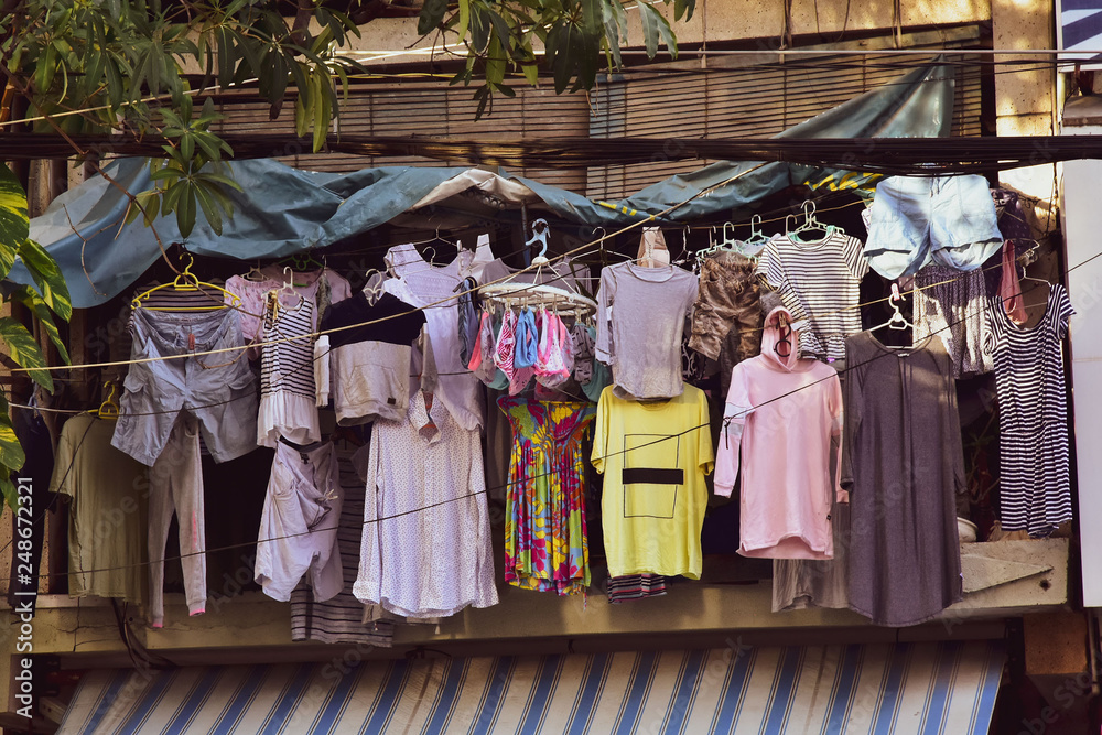Clothes of different colors weigh on hangers at a street shop, open second-hand showcase