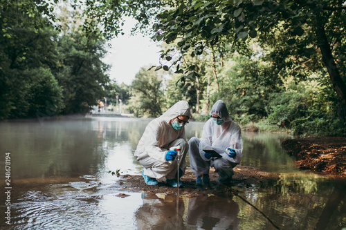 Tablou canvas Two scientists in protective suits taking water samples from the river