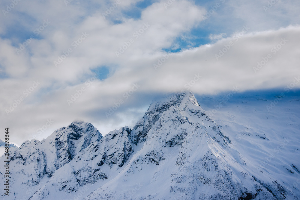 mountain peaks of Dombai mountains covered with snow surrounded by thick clouds against the blue sky