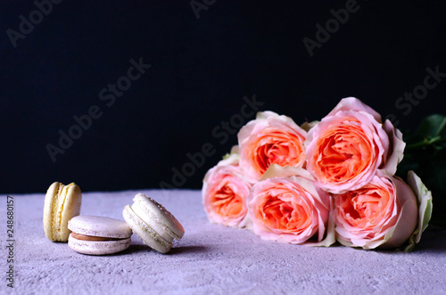 A stack of macaroons with a bouquet of beautiful peach-colored roses. photo