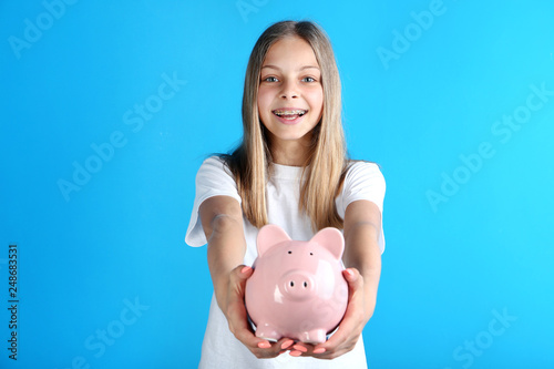 Young girl with piggy bank on blue background photo