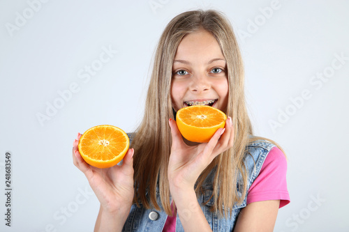 Young smiling girl with orange fruit on grey background