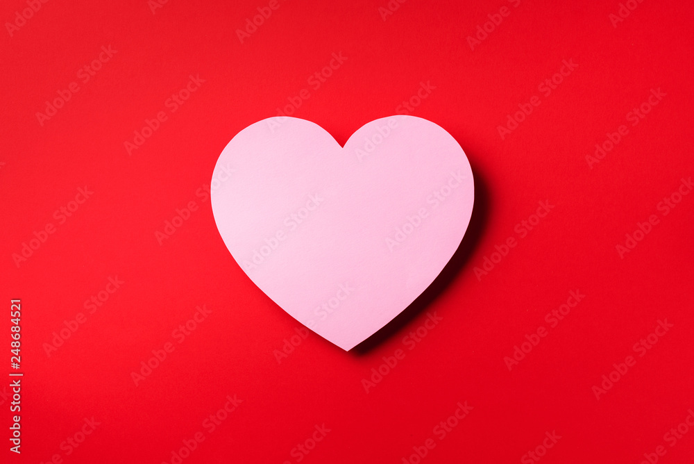 Pink heart cutted from paper over red background with copy space. Top view. Valentine's Day. Love, date, romantic concept.