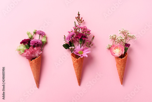 Summer minimal concept. Ice cream cone with pink flowers and leaves on punchy pastel background. Flat lay. Top view. Creative layout
