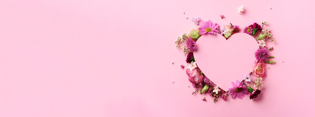 Creative layout with pink flowers, paper heart over punchy pastel background. Top view, flat lay. Spring, summer or garden concept. Present for Woman day. Banner