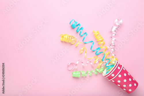 Colorful paper cups with ribbons on pink background