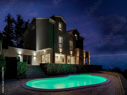 night view of the exterior of a modern villa in the foreground illuminated swimming pool