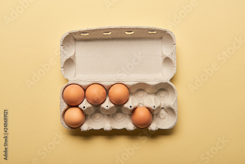 top view of brown organic eggs in cardboard box on yellow background