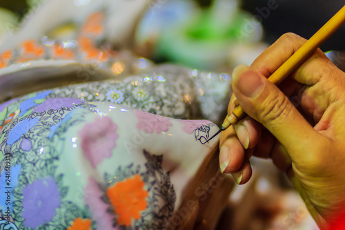 Close up hand of Thai woman artist during painting the masterpiece of Benjarong patterns, the famous thai 5- colored porcelain ceramic wares.