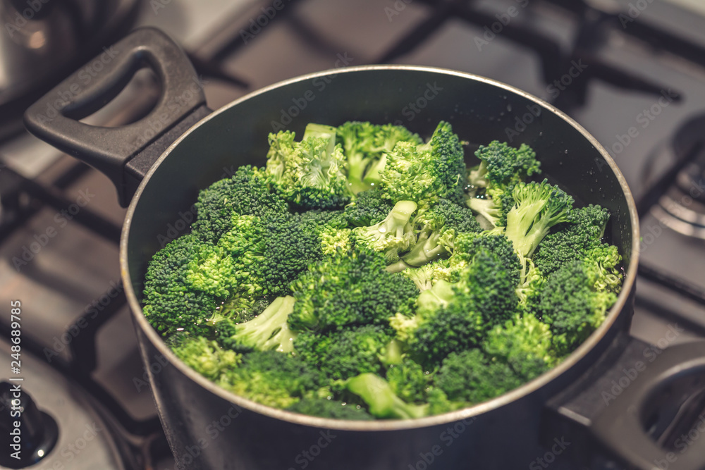 Pieces of fresh broccoli in water in a pot on stove, closeup, healthy eating or cooking concept Pieces of fresh broccoli in water in a pot on stove, closeup, healthy eating or cooking concept