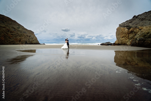 Adorable wedding couple walking along the beach  reflecting in the water.