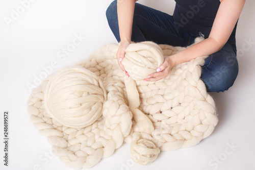 Blanket made of Merino wool and yarn balls on white background. Women's hands holding a ball. © Natalia
