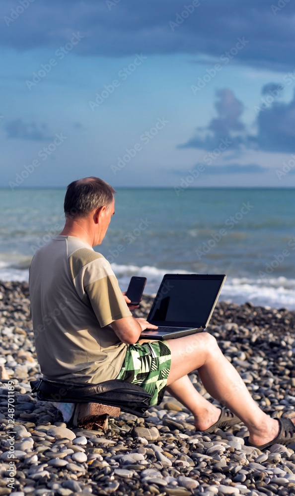 a man works in nature in a laptop, communicates over the phone with partners