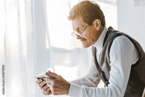 sad pensioner with mustache looking at photo in photo frame while sitting at home