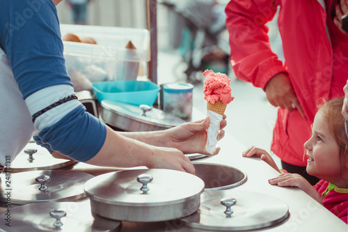 Little girl waiting for icecream. Mom buying a icecream her little daughter in a candy shop by the street photo