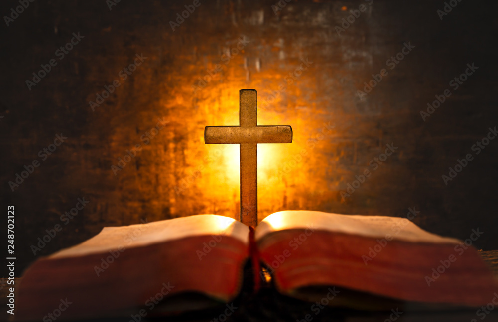 Close up cross and bible with light of candle background on wooden table. christian concept.