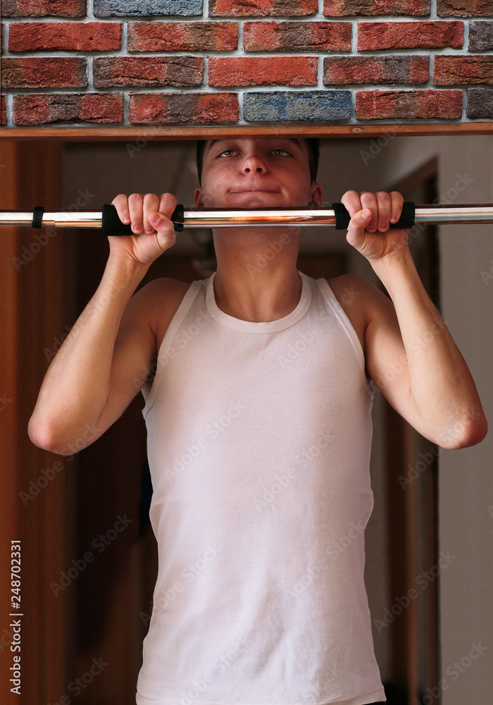 Young man executing exercise pulling up on horizontal bar at home Young man executing exercise pulling up on horizontal bar at home