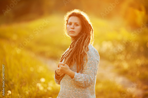 Girl with dreadlocks standing in the middle of the meadow