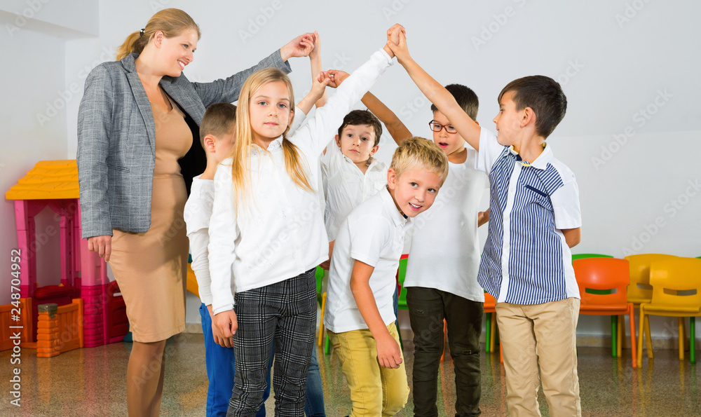 Fototapeta premium Positive female teacher playing circle game with children in classrom