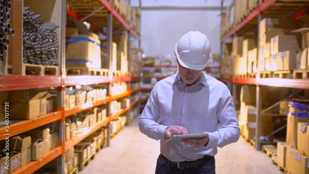 employee male warehouse worker engineer man in hard hat working at construction site warehouse, walking in logistics center factory. engineer using tablet computer, architect businessman man indoors employee male warehouse worker engineer man in hard hat working at construction site warehouse, walking in logistics center factory. engineer using tablet computer, architect businessman man indoors