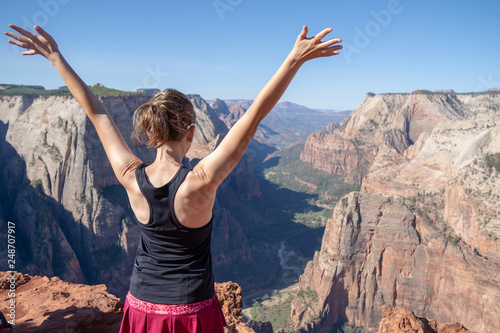 Adult female stands with back facing camera looking over Observation Point in Zion National Park in Utah, an 8 mile hike to the highest point in the park