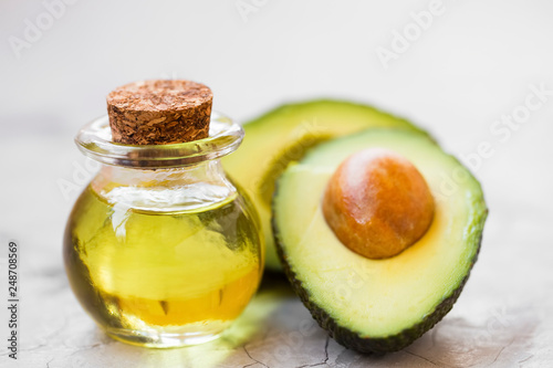 Avocado oil bottle closeup with half avocado fruit, green, aromatic ,fresh and healthy oil