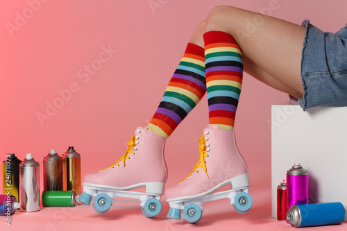 Woman with vintage roller skates and spray paint cans on color background, closeup