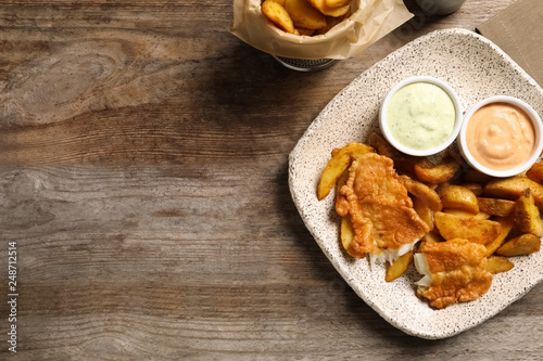 Plate with British traditional fish and potato chips on wooden background, top view. Space for text