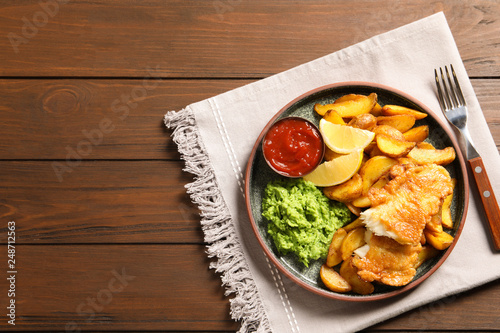 Plate with British traditional fish and potato chips on wooden background, top view. Space for text