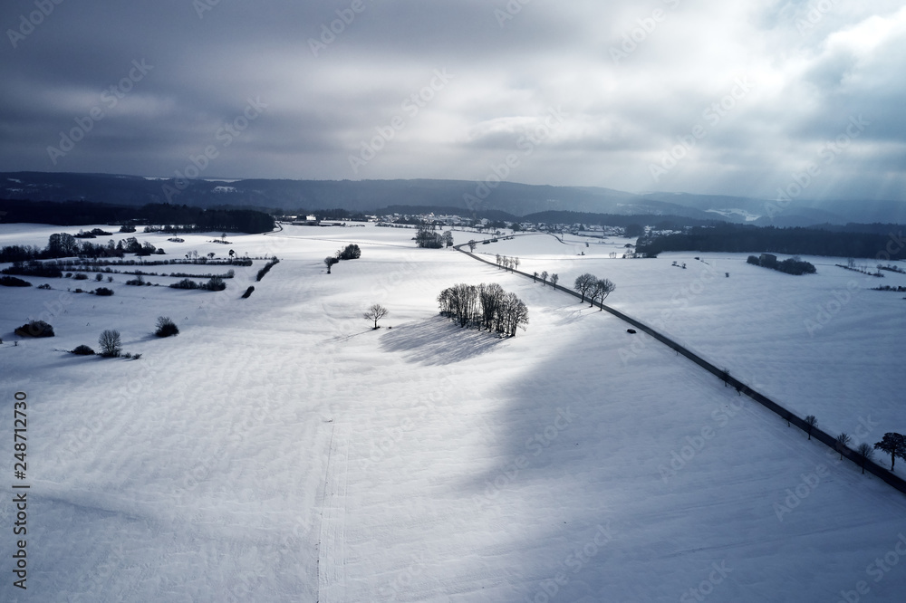 Aerial view of a winter curved road covered with snow. A snowy plateau with single trees captured from above with a drone.
