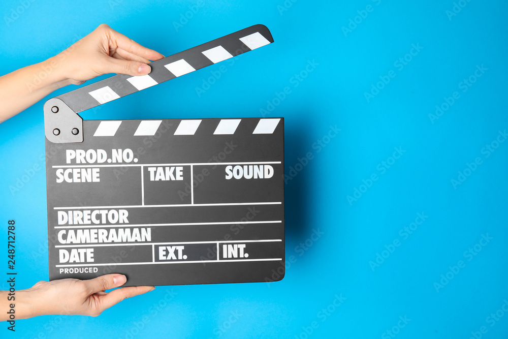 Woman holding clapperboard on color background, closeup with space for text. Cinema production