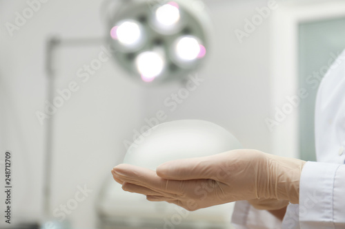 Doctor holding silicone implant for breast augmentation in clinic, closeup with space for text. Cosmetic surgery