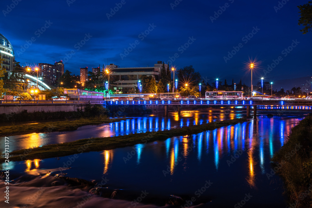 The city embankment and the bridge over the river, illuminated and decorated with lanterns on a summer night.