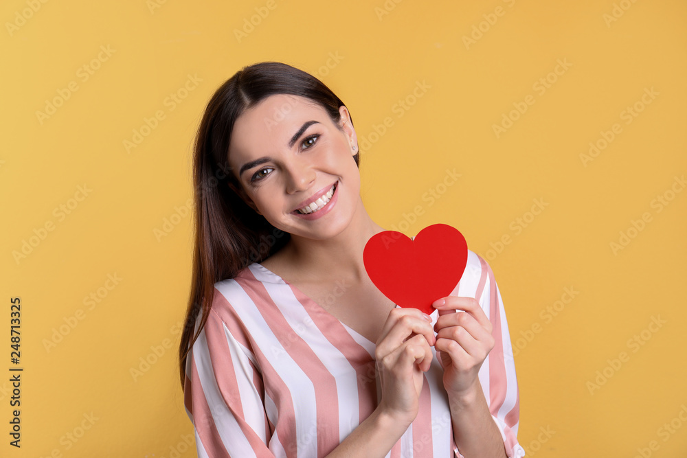 Portrait of young woman with paper heart on color background