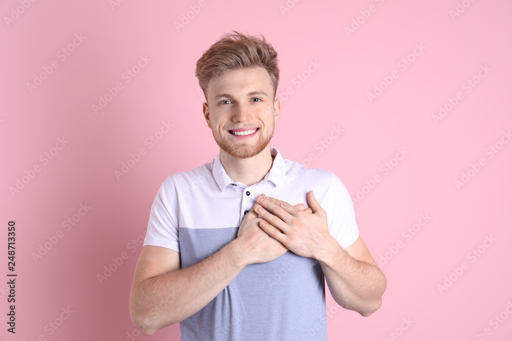Portrait of young man holding hands near heart on color background Portrait of young man holding hands near heart on color background