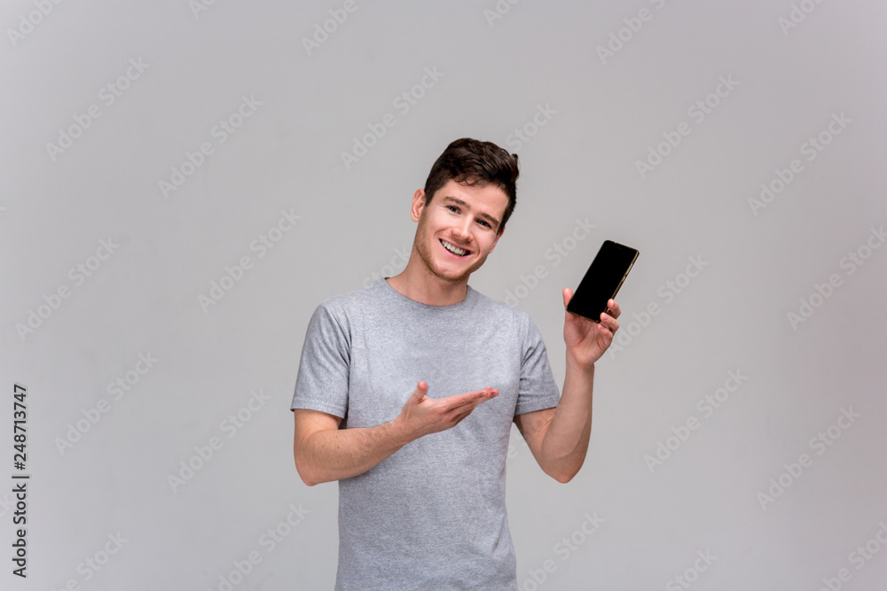 Smiling and laughing handsome young man use and show smartphone. isolate. grey t-shirt and blue jeans Smiling and laughing handsome young man use and show smartphone. isolate. grey t-shirt and blue jeans