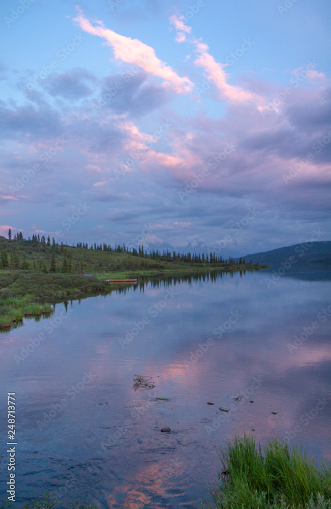 Pink clouds and trees reflected at sunset in Wonder Lake, Denali National Park, Alaska, USA.