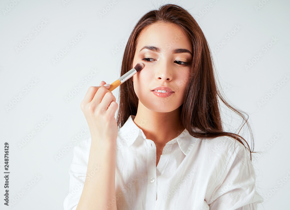 Make up brush in hand of smiling asian young woman with dark long hair on white background Make up brush in hand of smiling asian young woman with dark long hair on white background