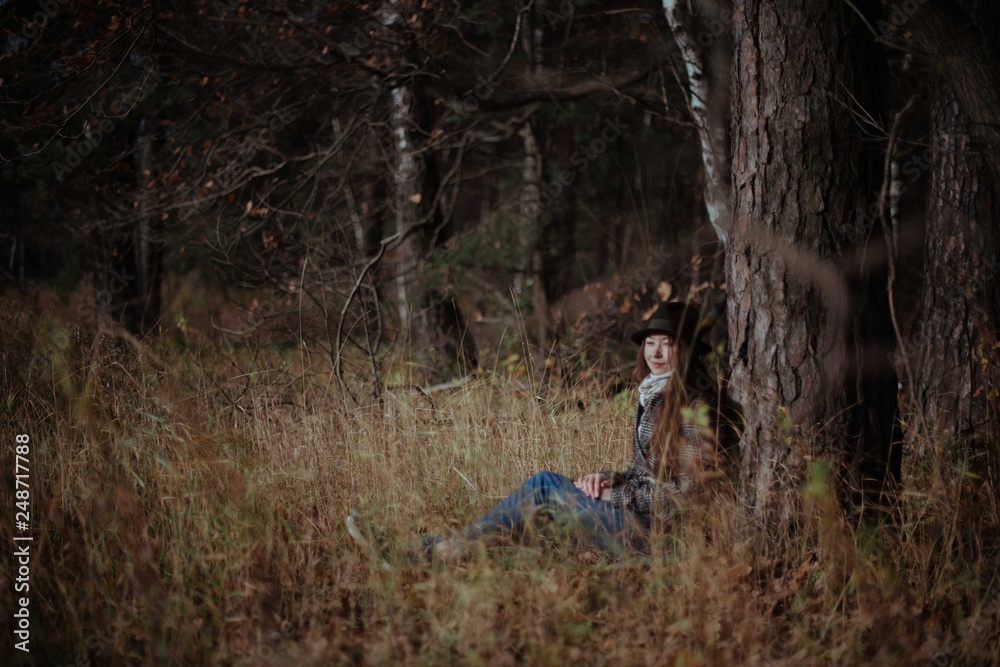 A girl sits alone under a tree in a forest on a sunny day. A girl sits alone under a tree in a forest on a sunny day.