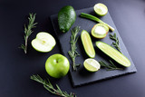 Green fruits and vegetables on dark slate board. Concept of natural green products. Avocado, kiwi, lime and apple on dark background. Rosemary, dill and chives on stone board