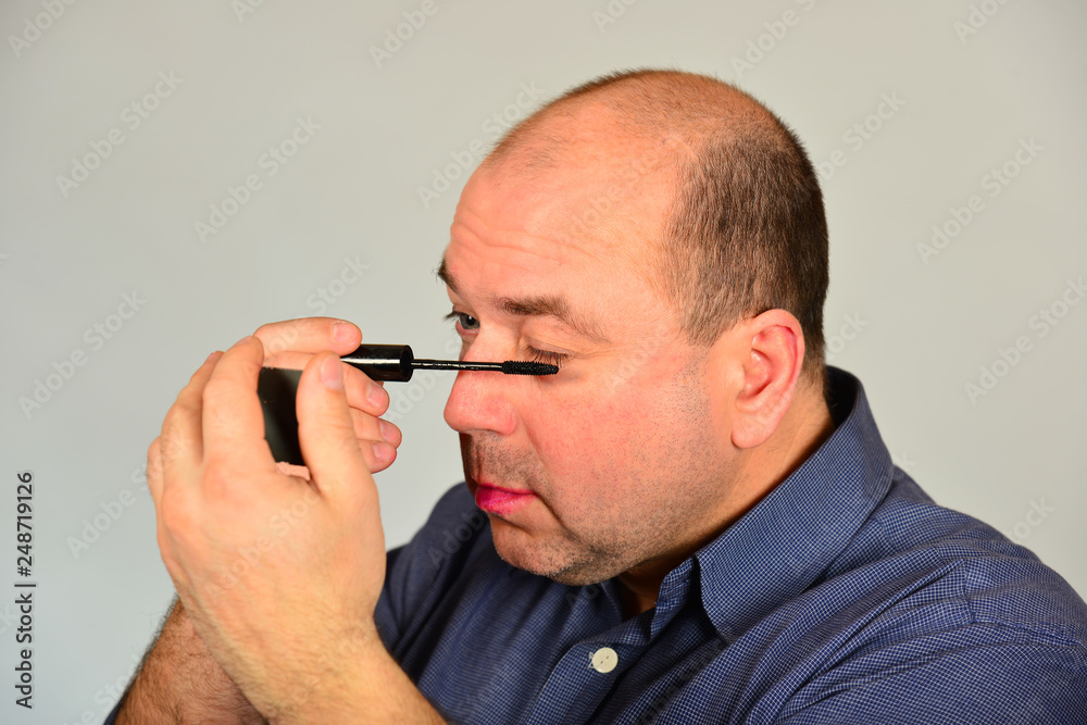An adult man paints his eyelashes in front of a mirror, getting ready for a date. An adult man paints his eyelashes in front of a mirror, getting ready for a date.