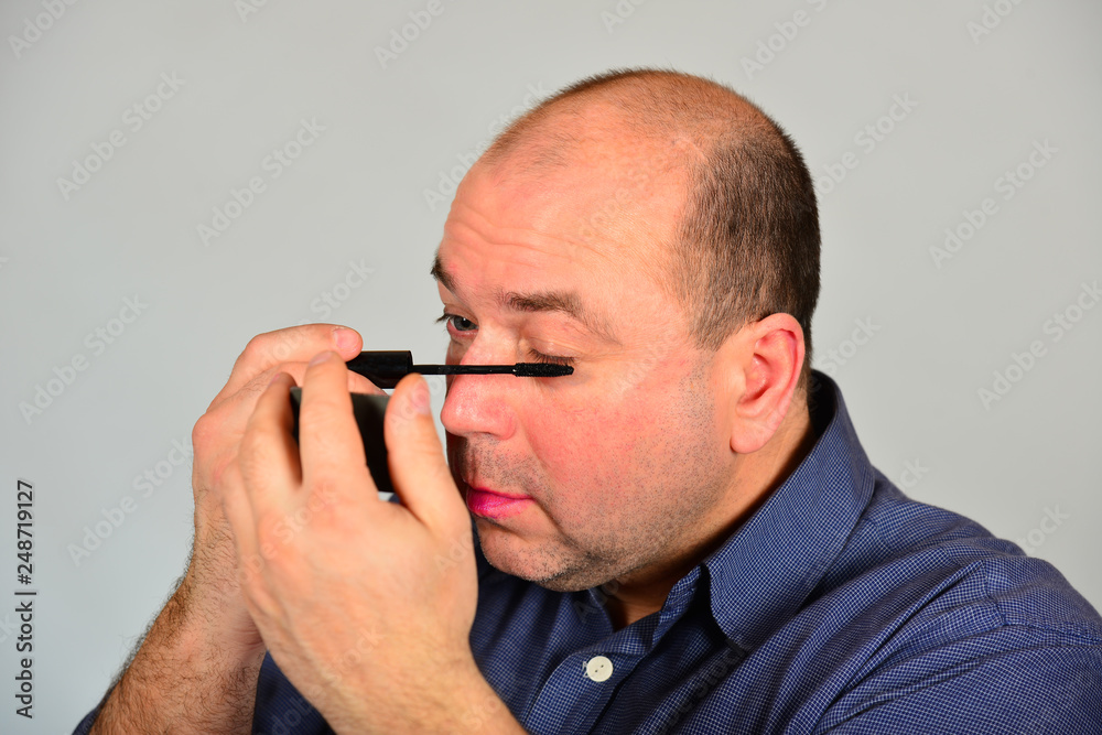 An adult man paints his eyelashes in front of a mirror, getting ready for a date. An adult man paints his eyelashes in front of a mirror, getting ready for a date.