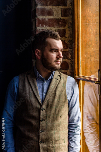 Photo of elegant smiling young man in a suit, on the background of vintage brickwall, looking in the old rustic window © J.Pliacushok
