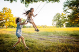 Mom swinging daughter on a swing in the field