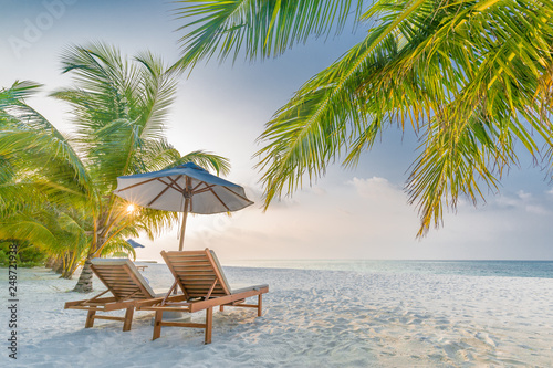 Tropical beach resort hotel background as summer landscape with lounge chairs and palm trees in sun rays and calm sea for beach banner. Luxury vacation and holiday destination concept