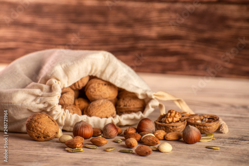 Almond nuts, hazelnuts, walnuts and sweet seeds in a burlap bag on a wooden background.